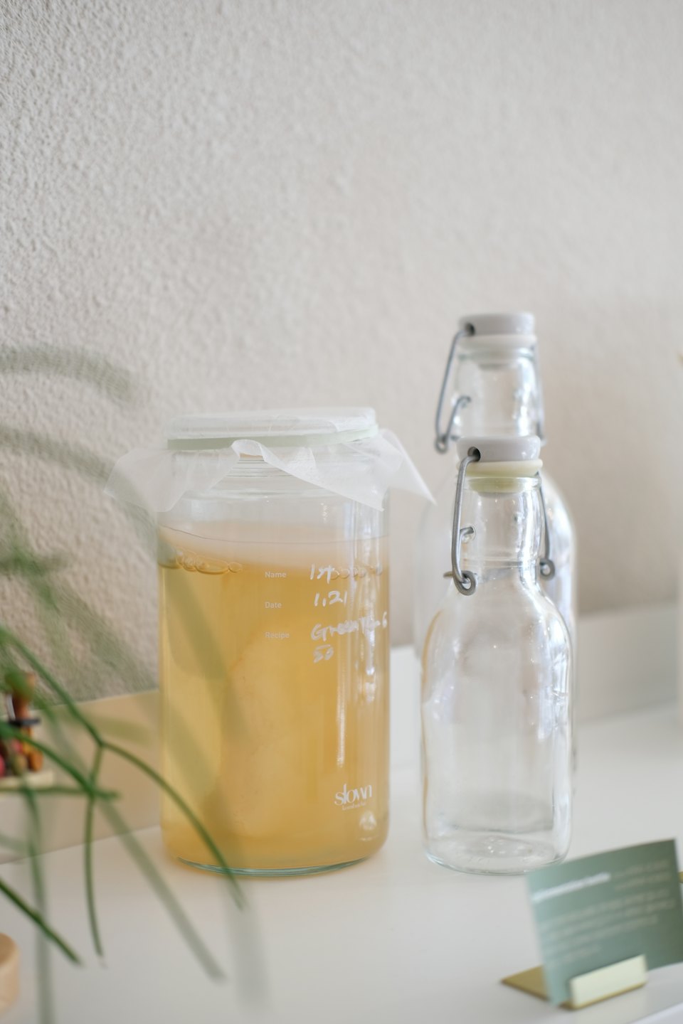 Tarro de fermentación de cristal con notas escritas a mano sobre superficie blanca.