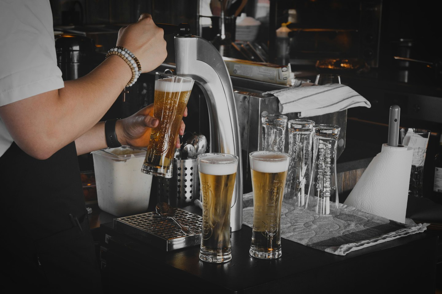 Un camarero sirve una cerveza dorada en un vaso alto.