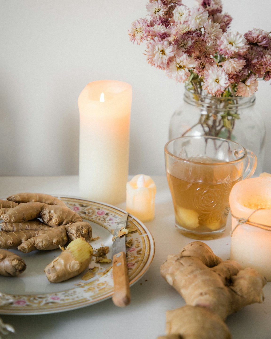 Raíces de jengibre fresco y té con velas sobre un plato decorativo.